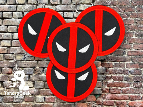 Four round patches with red borders and black backgrounds, featuring white, stylized eyes and a red diagonal line, are displayed against a brick wall backdrop. Logo: Tundra Geek Creations.