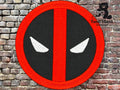 A circular patch with a red border and stripe, black background, and two white eye shapes, resembling the Deadpool logo, displayed against a brick wall background.