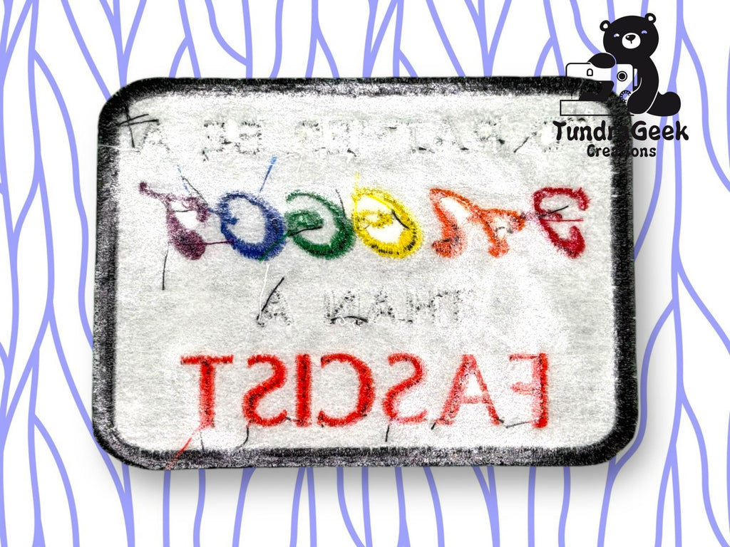 A rectangular patch reads “FASCIST” in red and “THAN A BIGOT” in rainbow colors, shown in reverse. A black bear and Tundra Geek Creations logo are in the top right corner.