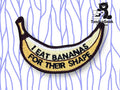 An embroidered patch shaped like a banana with the text I EAT BANANAS FOR THEIR SHAPE on it, displayed on a white background with purple wavy lines.