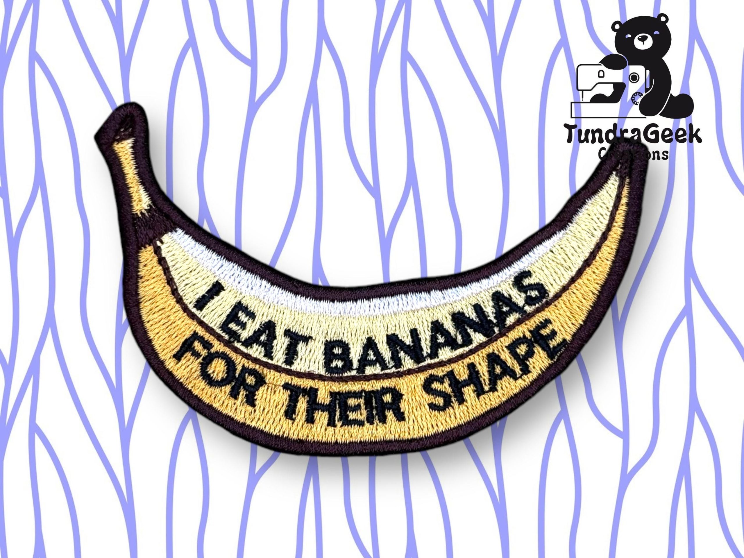 An embroidered patch shaped like a banana with the text I EAT BANANAS FOR THEIR SHAPE on it, displayed on a white background with purple wavy lines.