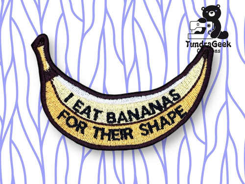 An embroidered patch shaped like a banana with the text I EAT BANANAS FOR THEIR SHAPE on it, displayed on a white background with purple wavy lines.