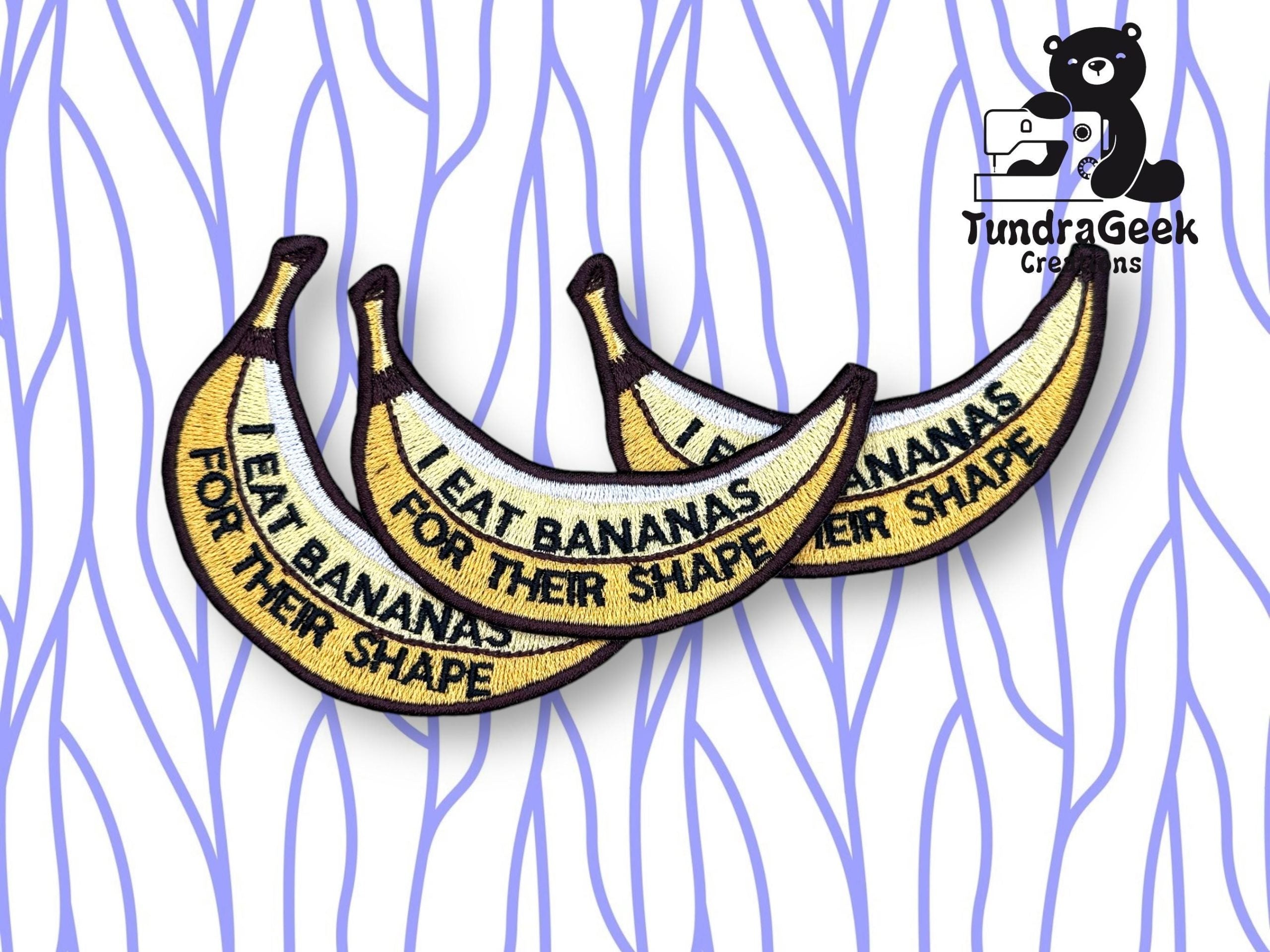 Three embroidered patches shaped like banana peels, each with the text I eat bananas for their shape, displayed on a white background with blue wavy lines. TundraGeek Creations logo in corner.