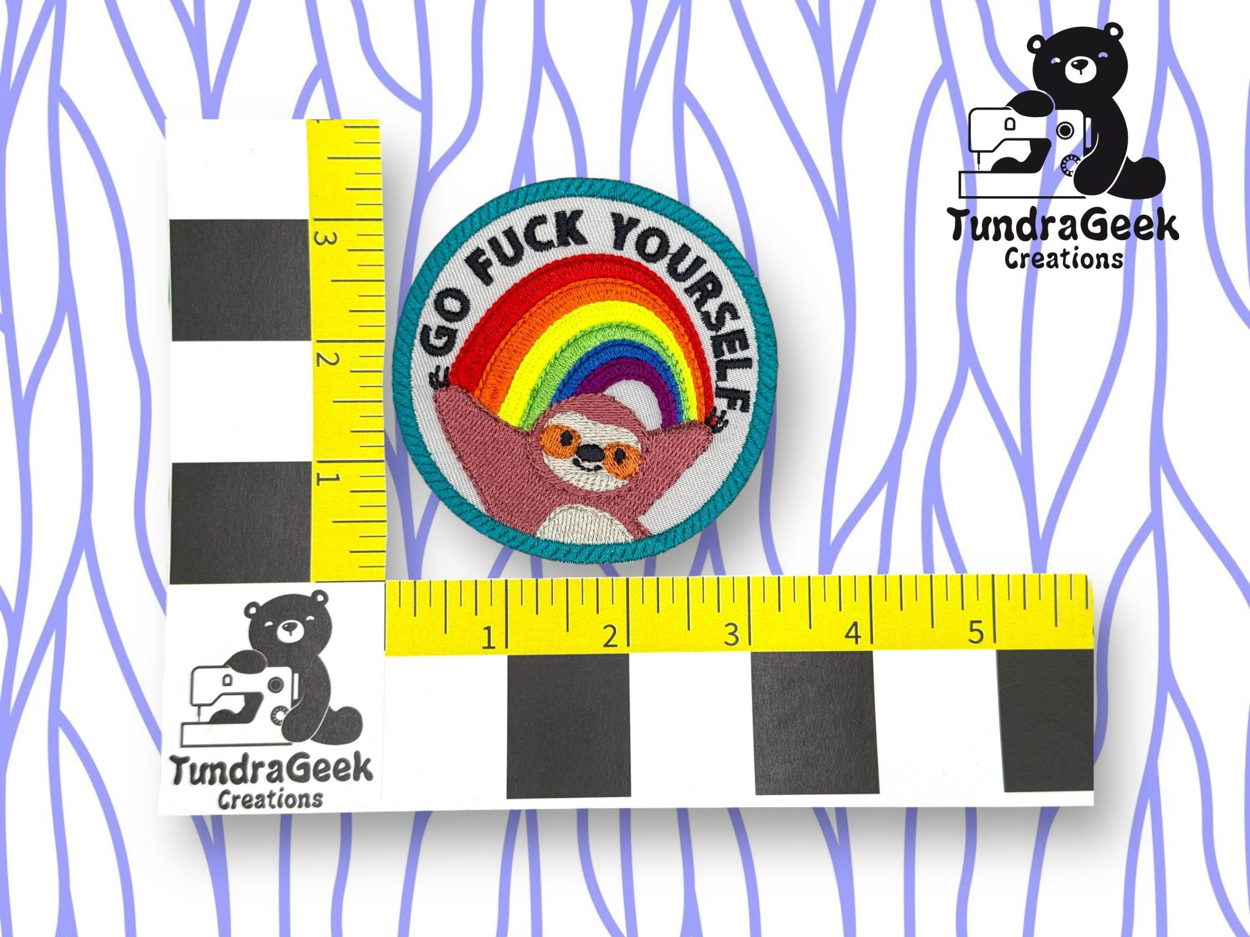 A circular patch showing a sloth under a rainbow with the text GO FUCK YOURSELF, placed between two rulers and featuring the TundraGeek Creations logo.