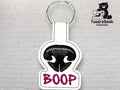 A white keychain with black embroidery of a bear nose above the word BOOP in purple, displayed against a white brick wall with a TundraGeek Creations logo.