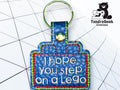 A blue keychain shaped like a Lego brick displays the embroidered text I hope you step on a Lego. A TundraGeek Creations logo is in the top right corner.