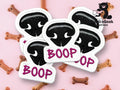Five embroidered patches with a black animal nose and the word BOOP in pink, placed on a pink background with dog bone treats.