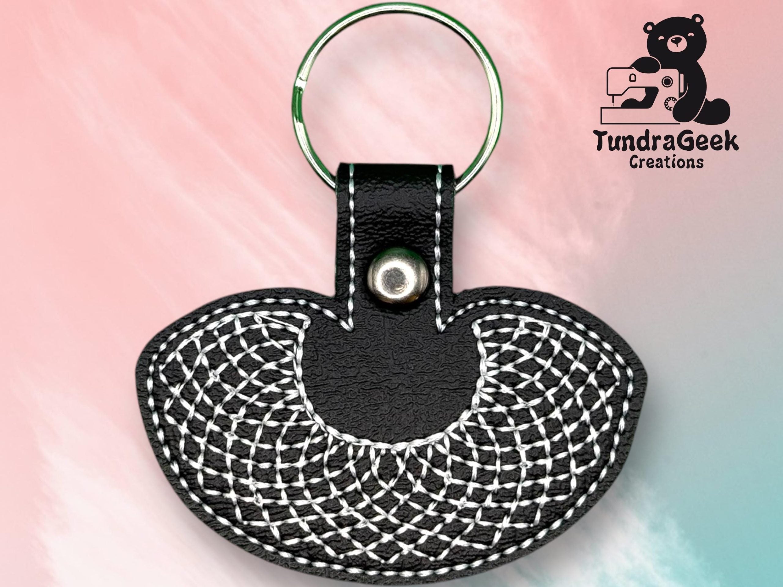A black faux leather keychain with white geometric stitching, metal snap, and keyring, shown against a pink and blue background with the TundraGeek Creations logo in the corner.