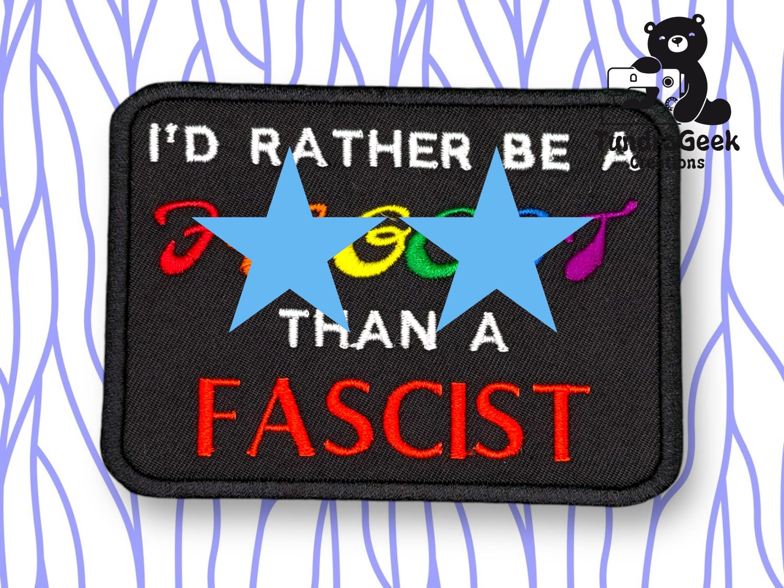 A rectangular patch with text reading ID RATHER BE A [censored] THAN A FASCIST. Part of the word is obscured by two blue stars. A cartoon bear is in the top right corner.