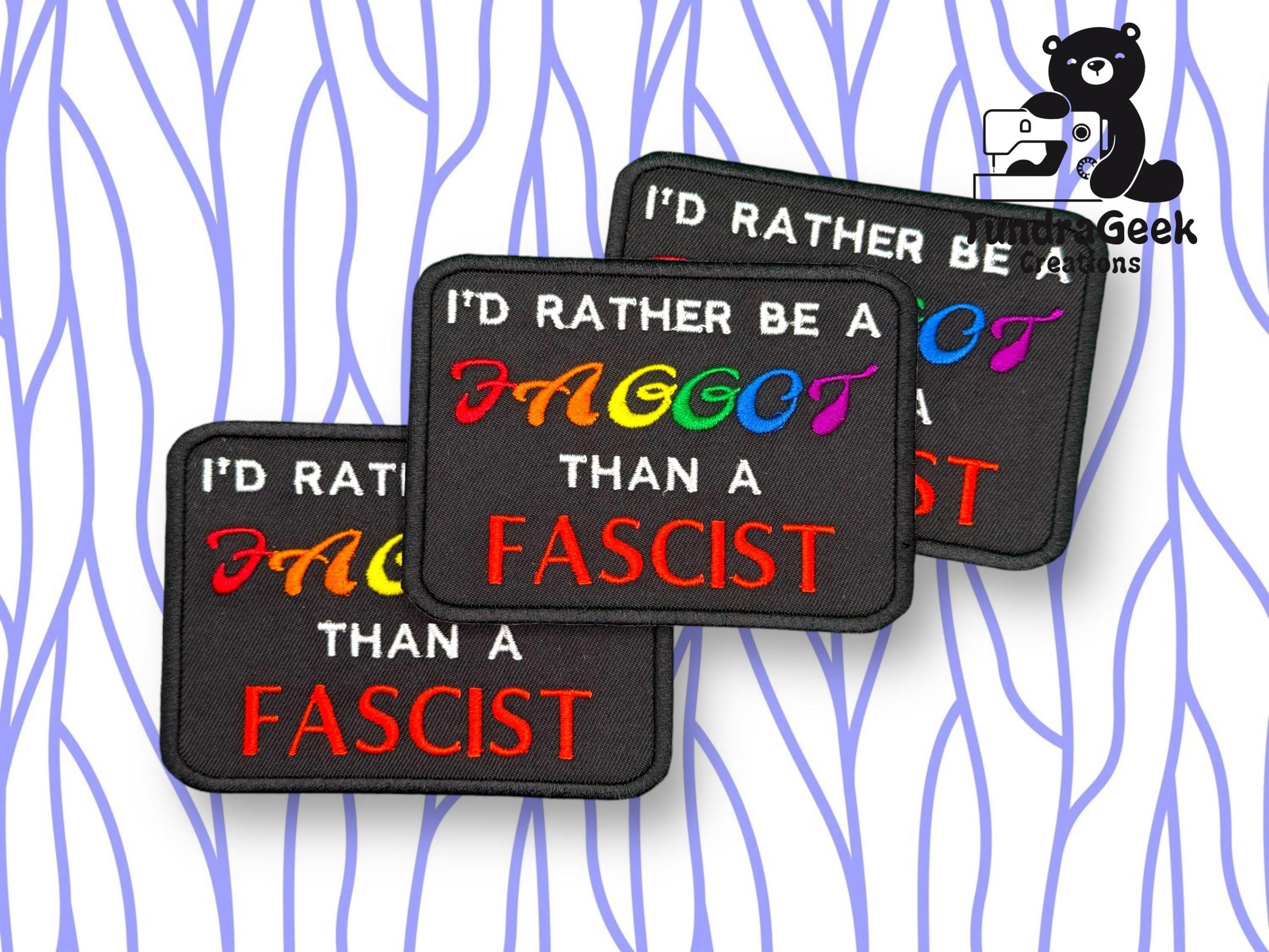 Three rectangular patches read ID RATHER BE A FAGGOT THAN A FASCIST, with FAGGOT in rainbow letters and FASCIST in red, against a white background with blue wavy lines.