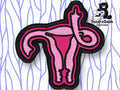 An embroidered pink patch shaped like a uterus with fallopian tubes, outlined in black, displayed on a patterned background. TundraGeek Creations logo is in the top right corner.