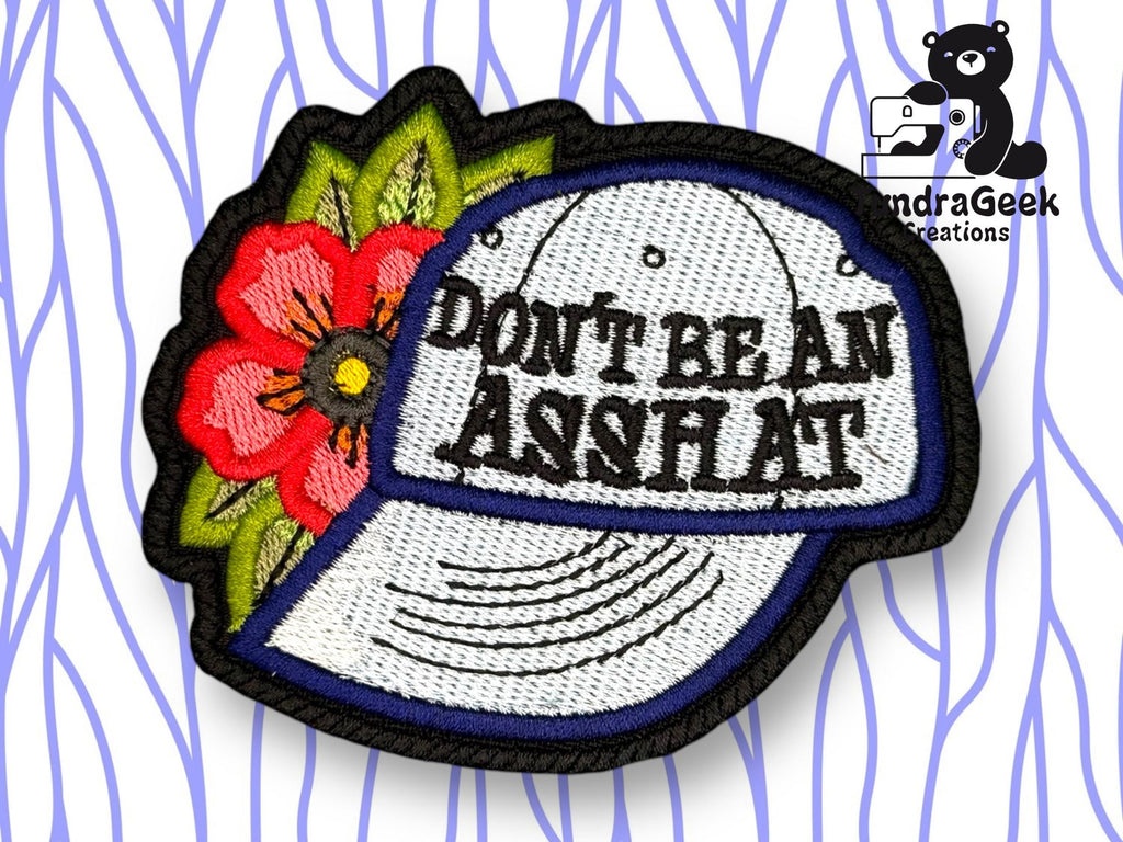 An embroidered patch shows a white baseball cap with the words DONT BE AN ASSHOLE, next to a red flower with green leaves, with a SondraGeek Creations logo in the corner.