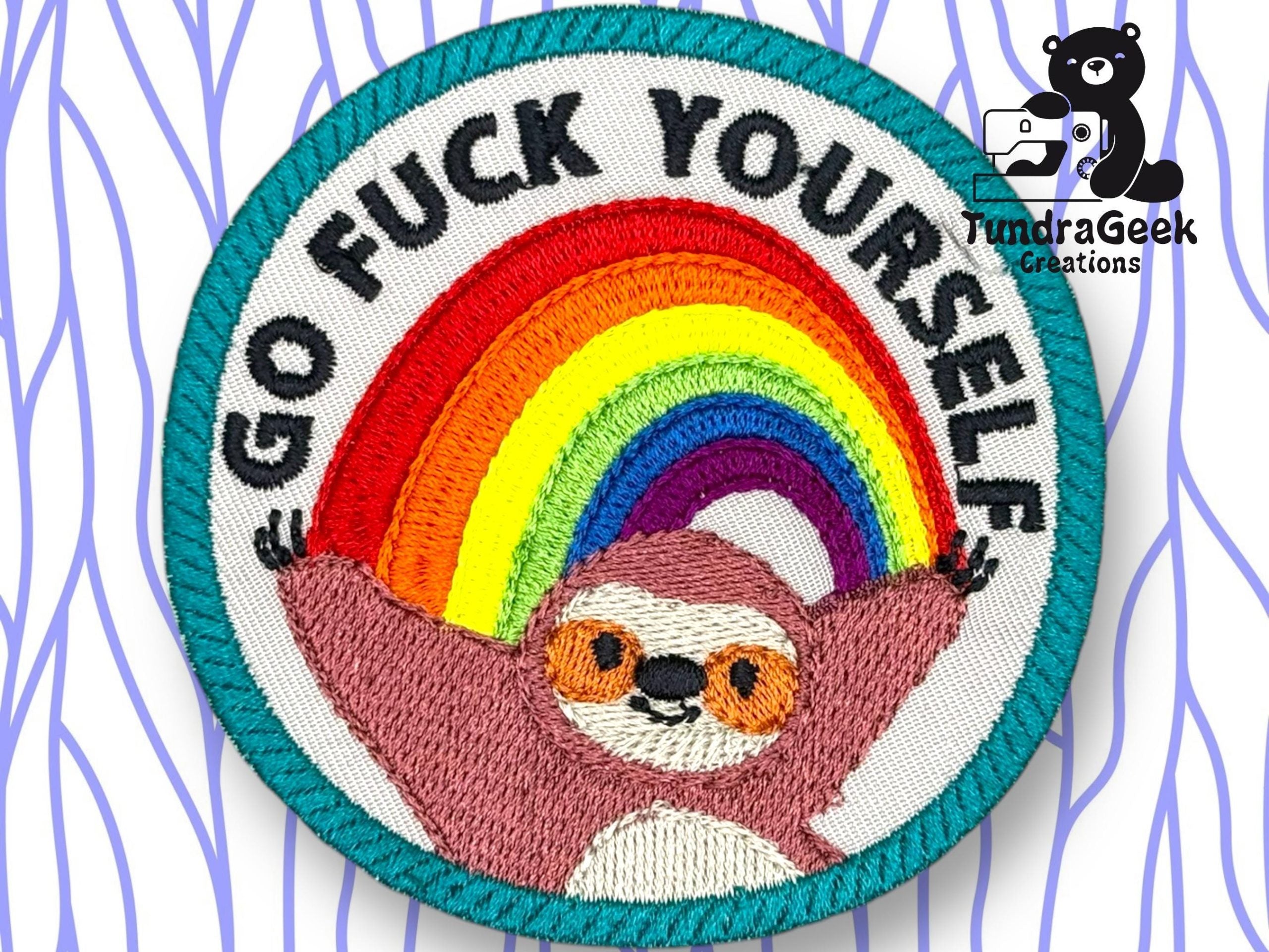A circular embroidered patch shows a smiling sloth under a rainbow with the text GO FUCK YOURSELF above. Background features a blue wavy pattern and the TundraGeek Creations logo.