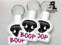 Three keychains with black embroidered dog noses and the word BOOP in purple text, displayed against a light brick background with a TundraGeek Creations logo.