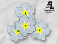 Four embroidered blue flowers with yellow and green centers are arranged on a light geometric background, with a TundraGeek Creations logo featuring a bear holding a sewing machine in the top right corner.
