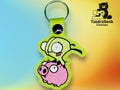 A green keychain featuring an embroidered cartoon of a green character riding a pink pig, with the TundraGeek Creations logo in the corner.