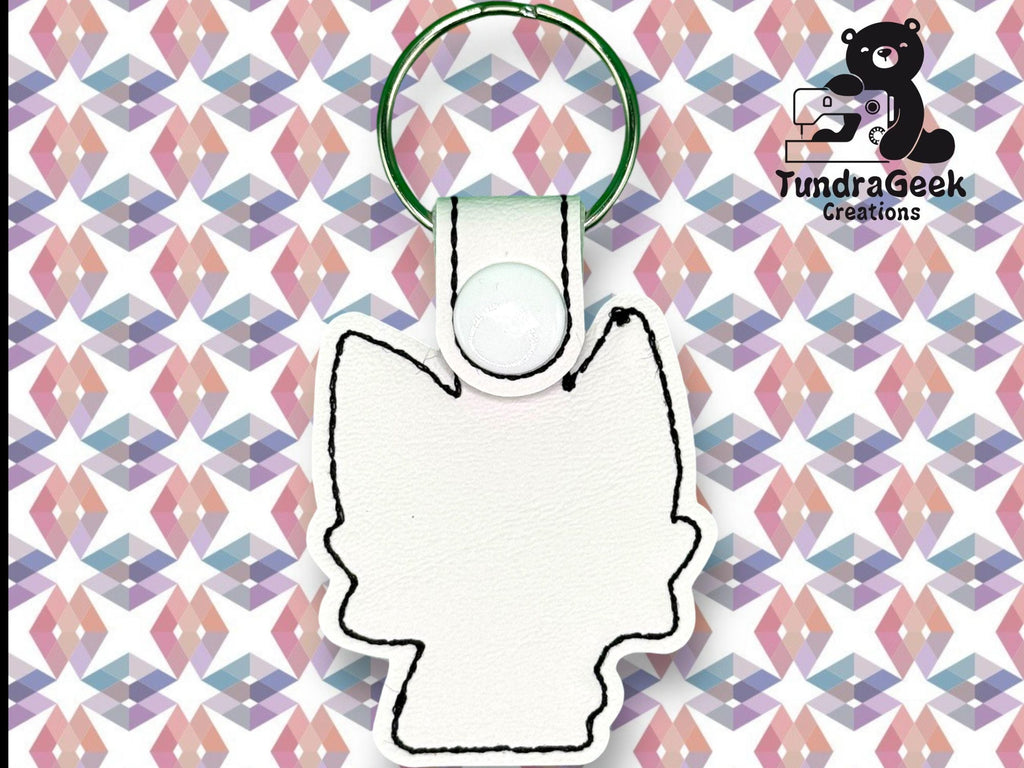 White keychain in the shape of an animal head with black stitching, displayed on a geometric patterned background. TundraGeek Creations logo is in the top right corner.