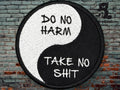 A round patch with a yin-yang design features the phrases Do No Harm on the white half and Take No Shit on the black half, placed against a brick wall background.