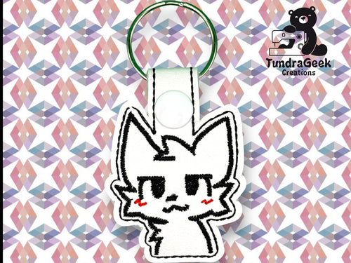 A white keychain with a cartoon cat face and red cheeks is displayed on a geometric pastel background. Logo in the corner reads TundraGeek Creations with a bear and sewing machine icon.