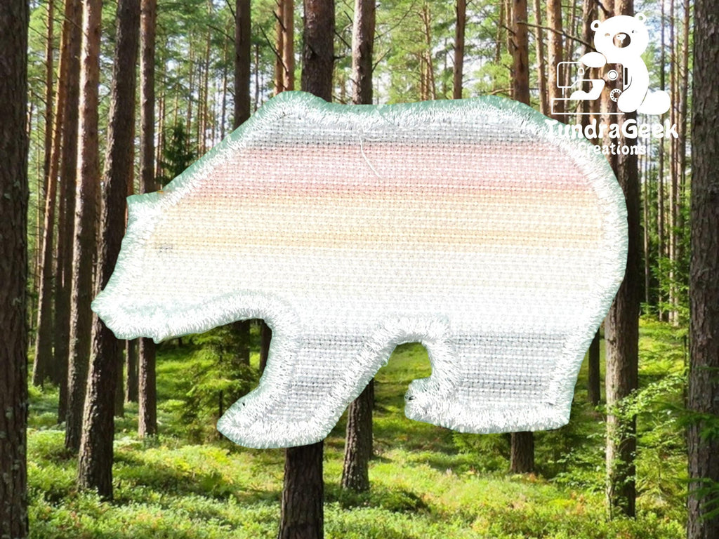 A bear-shaped fabric patch with pastel stripes and a metallic border is superimposed on a forest background. The Tundra Geek Creations logo is in the upper right corner.