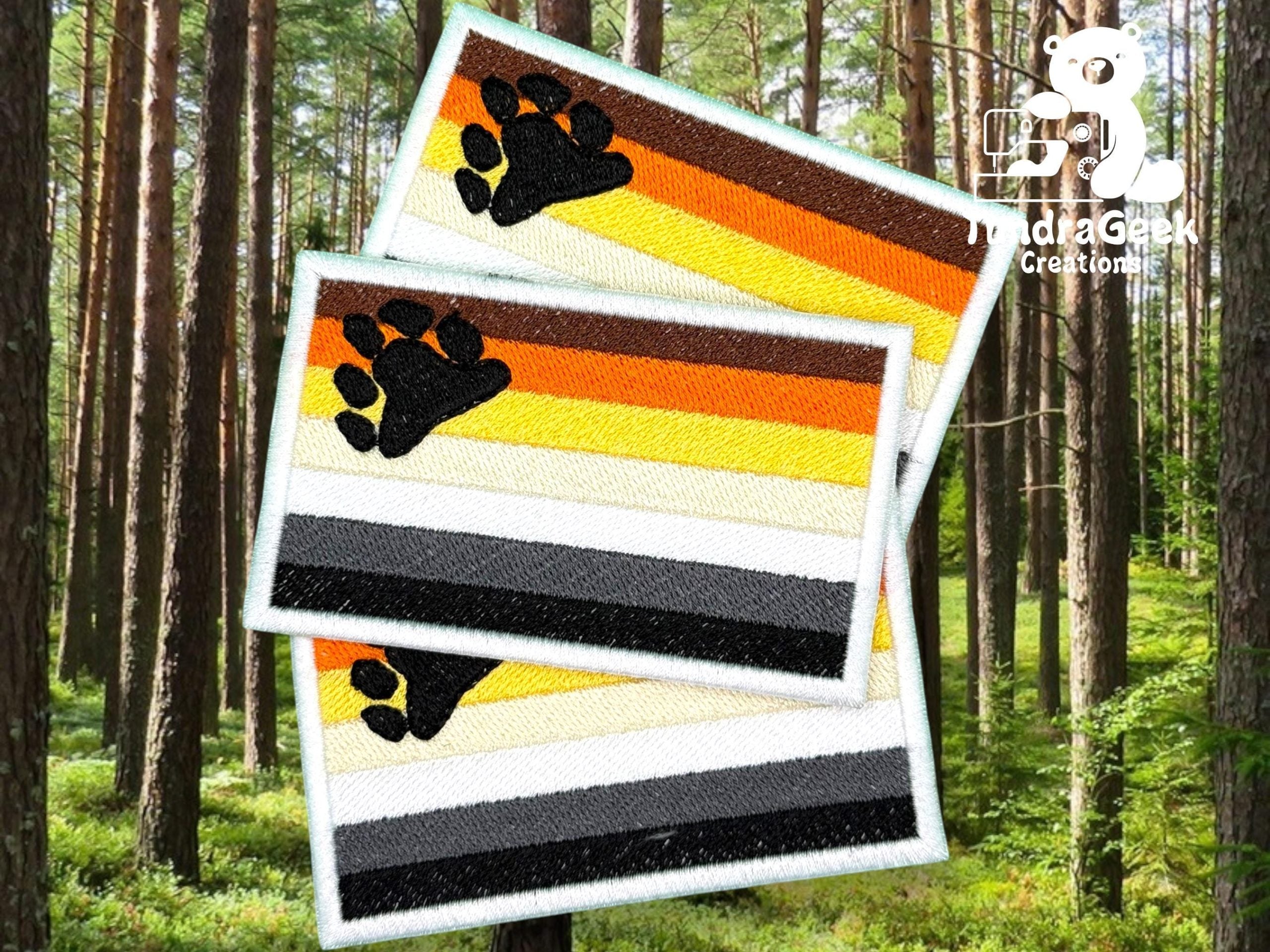 Three rectangular embroidered patches with bear paw prints and horizontal stripes in brown, orange, yellow, white, gray, and black are displayed against a forest background.