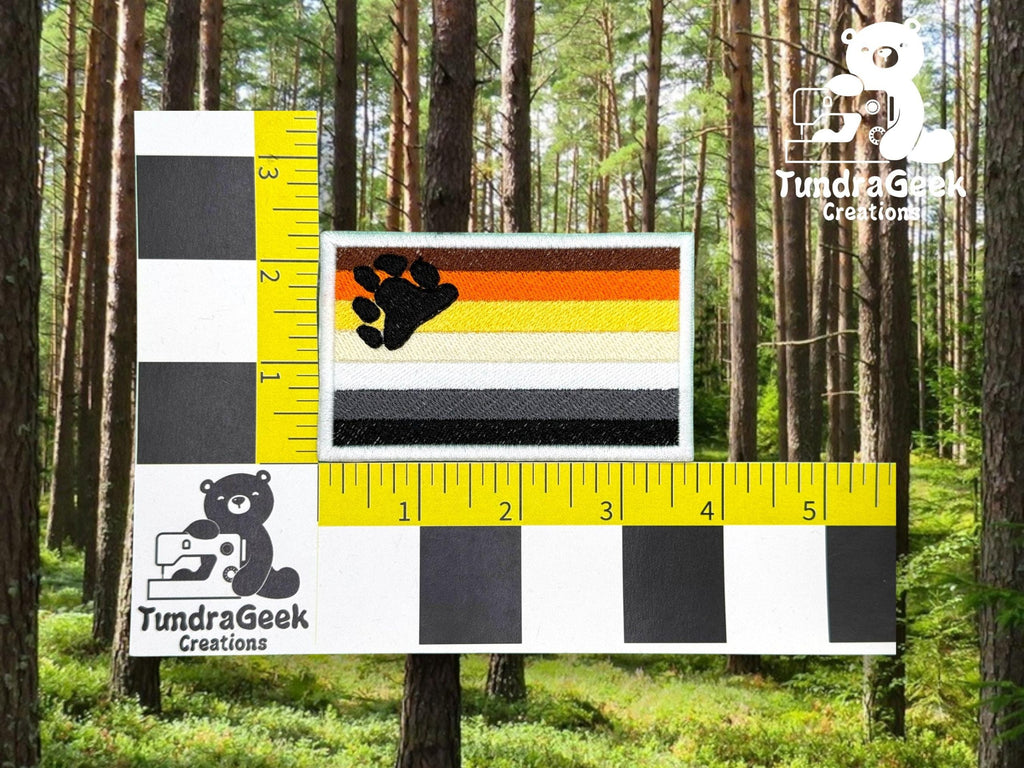 A rectangular patch with horizontal stripes and a black paw print, shown next to a ruler for scale, displayed against a forest background.