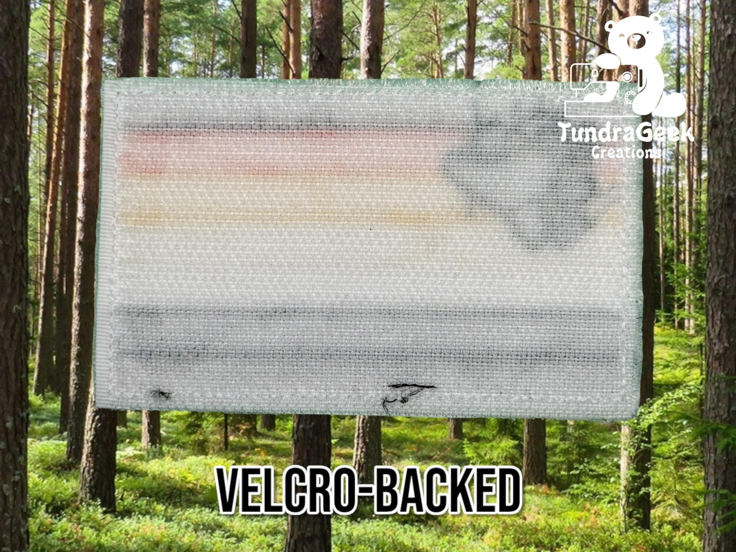 A rectangular velcro-backed patch with faded colors and blurred design, displayed against a forest background. Text: VELCRO-BACKED and TundraGeek Creations.