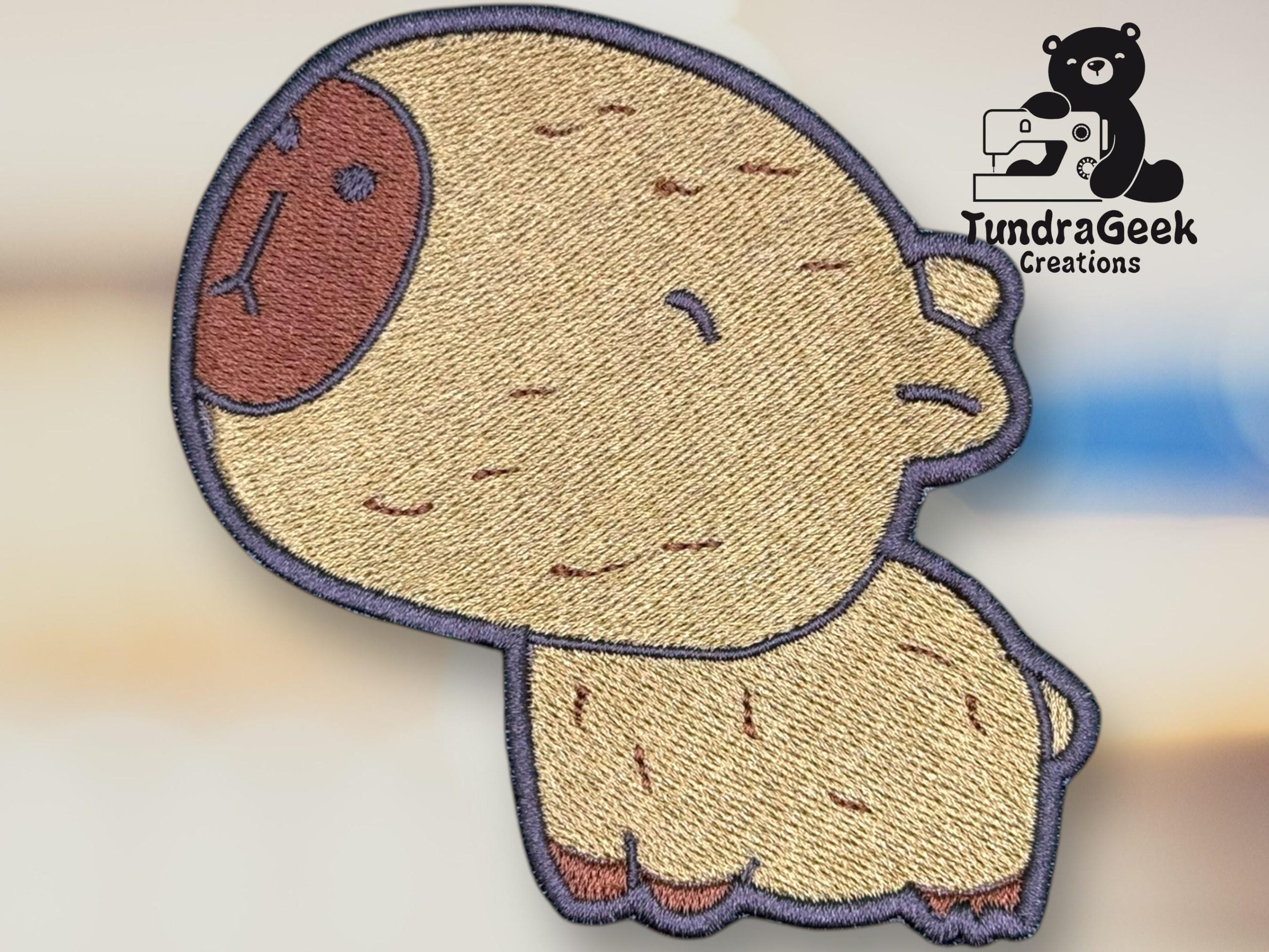 Embroidered patch depicting a cute, cartoon-style animal resembling a sheep with a large brown face. The TundraGeek Creations logo is visible in the top right corner.