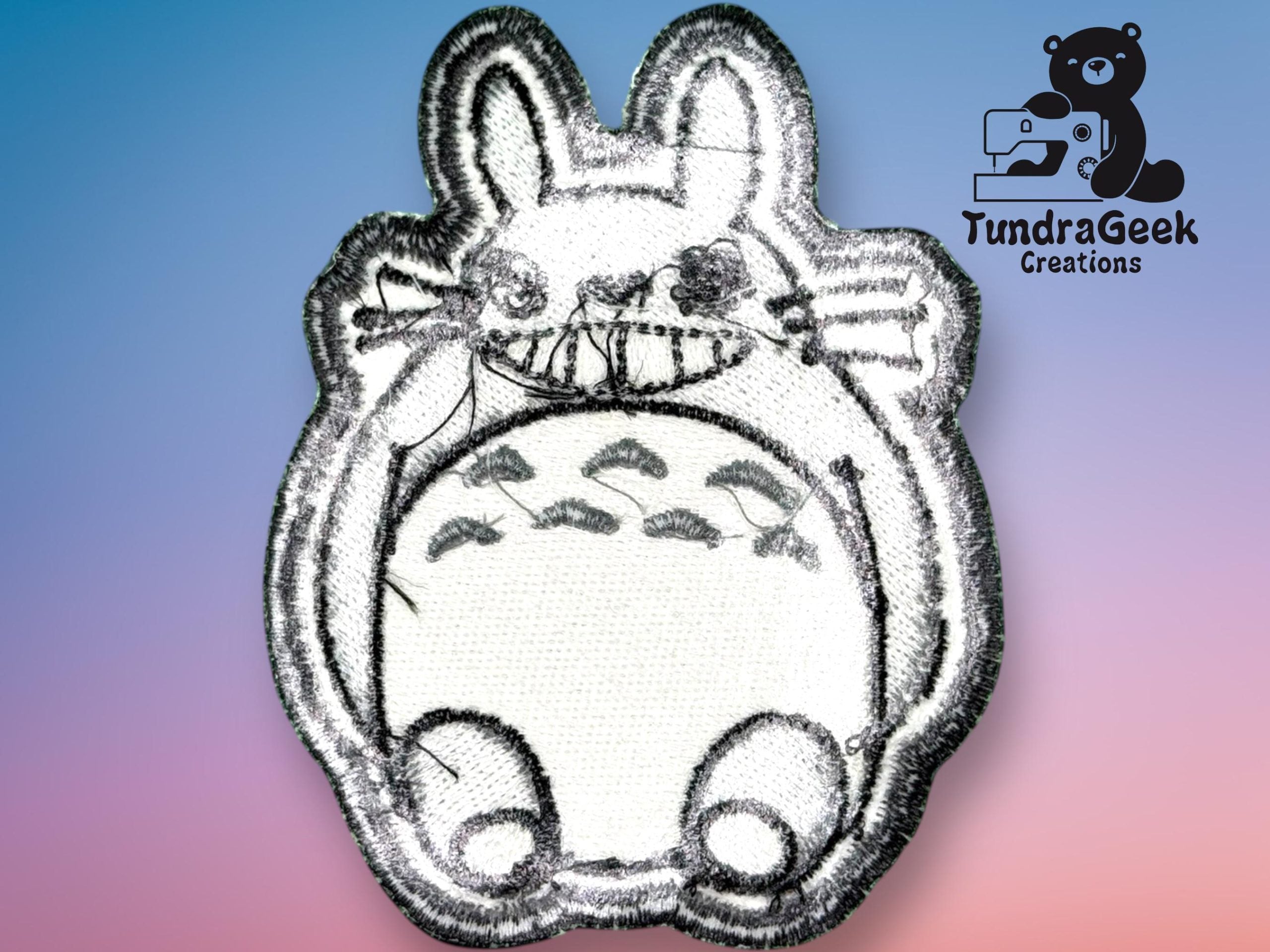 An embroidered patch resembles Totoro, a character from Studio Ghibli, on a gradient background with the TundraGeek Creations logo in the corner.