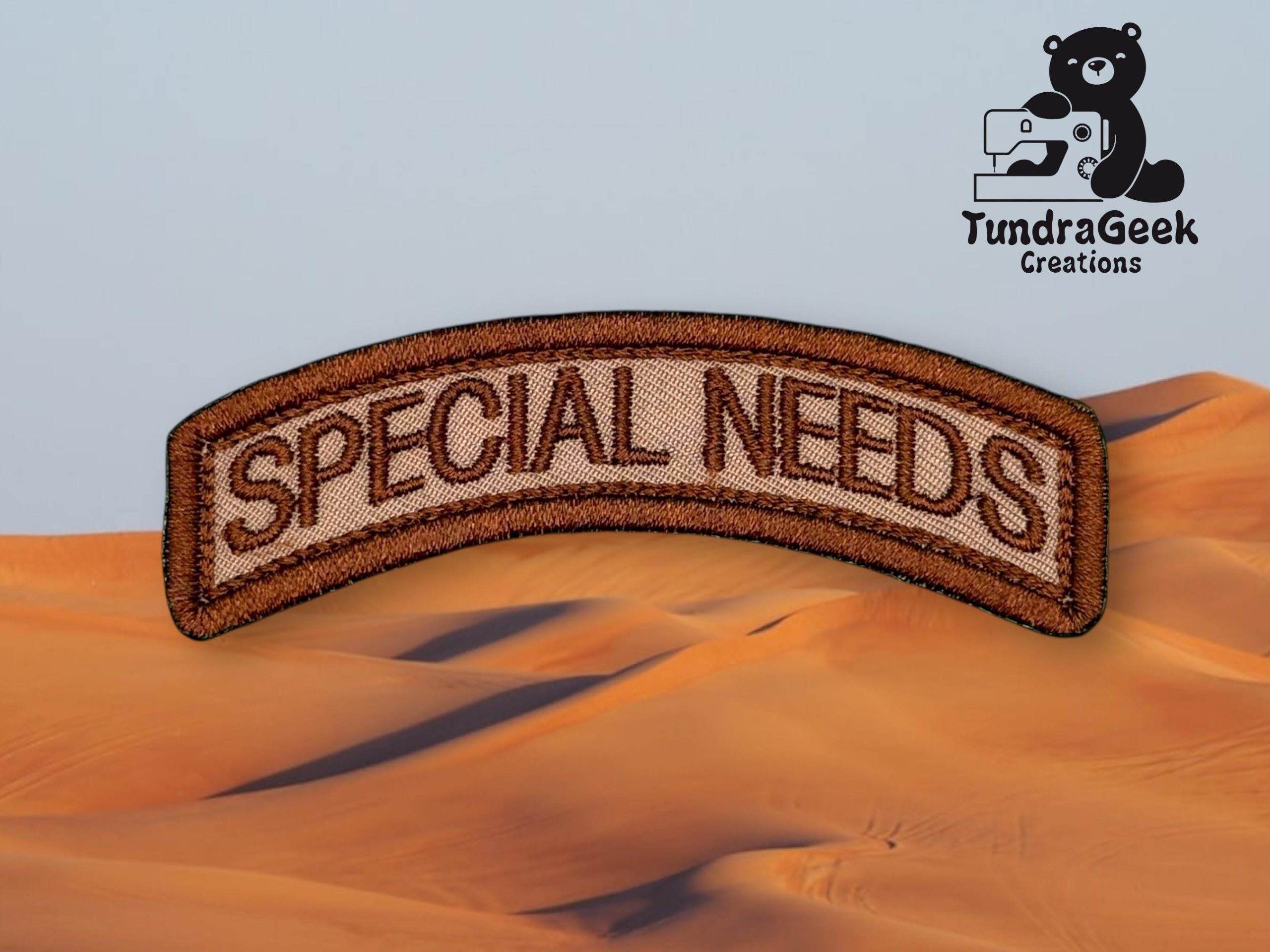 A brown embroidered patch reads SPECIAL NEEDS on a desert background, with the TundraGeek Creations logo featuring a bear holding a sewing machine in the upper right corner.