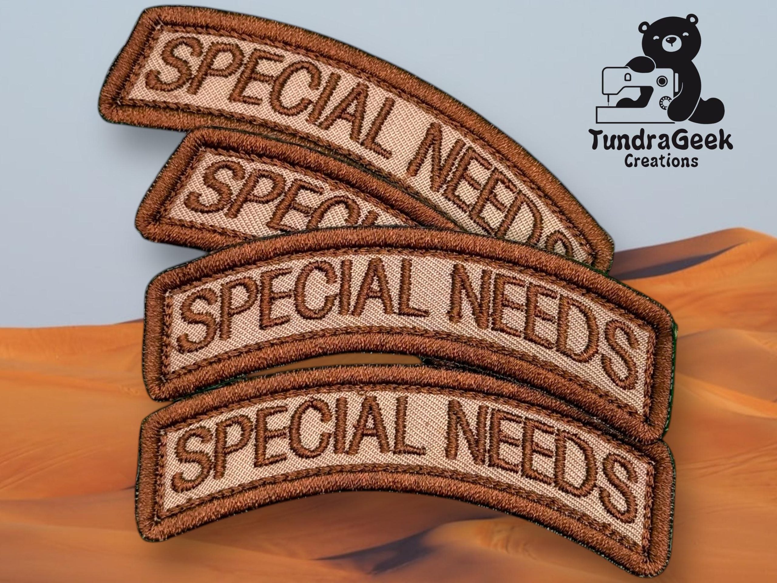 Four brown embroidered patches with the words SPECIAL NEEDS stacked on top of each other, with a TundraGeek Creations logo in the upper right corner.