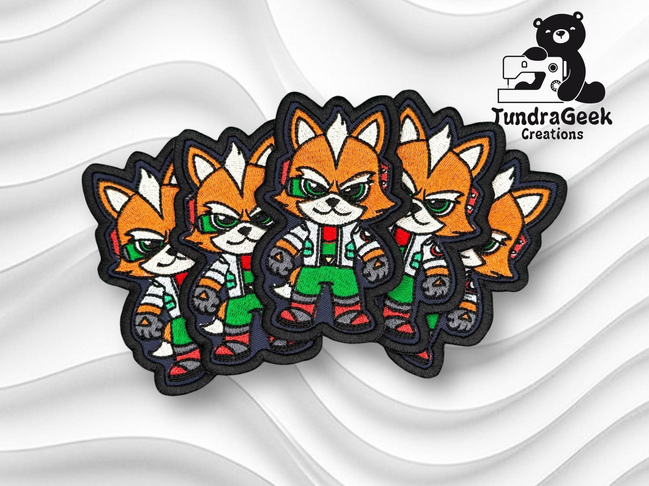 Four embroidered patches featuring an anthropomorphic fox character in a confident pose, displayed on a white textured background with the TundraGeek Creations logo in the top right corner.