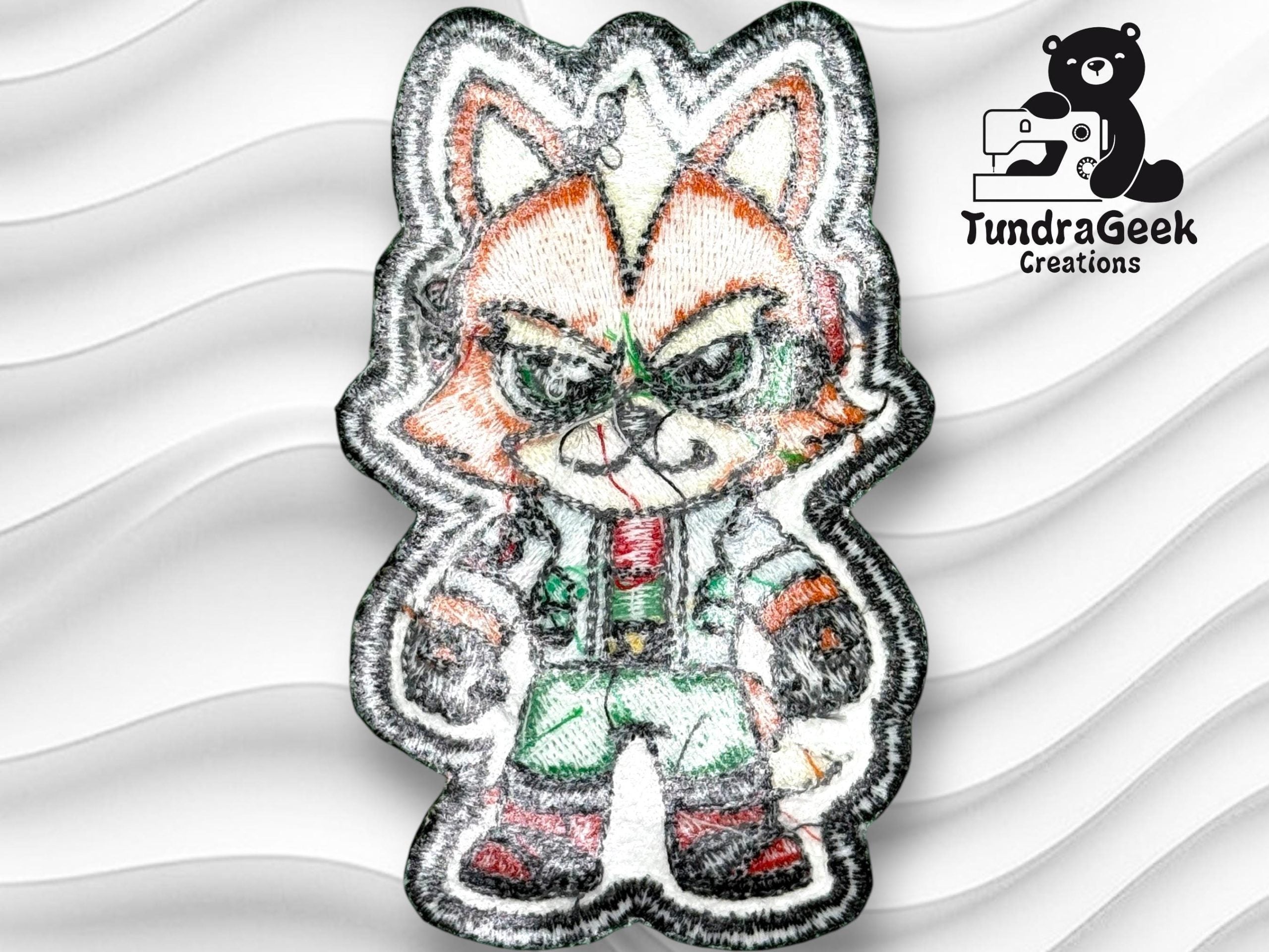 Embroidered patch of an anthropomorphic fox character in a green and white outfit, displayed on a wavy white background with the TundraGeek Creations logo in the top right corner.