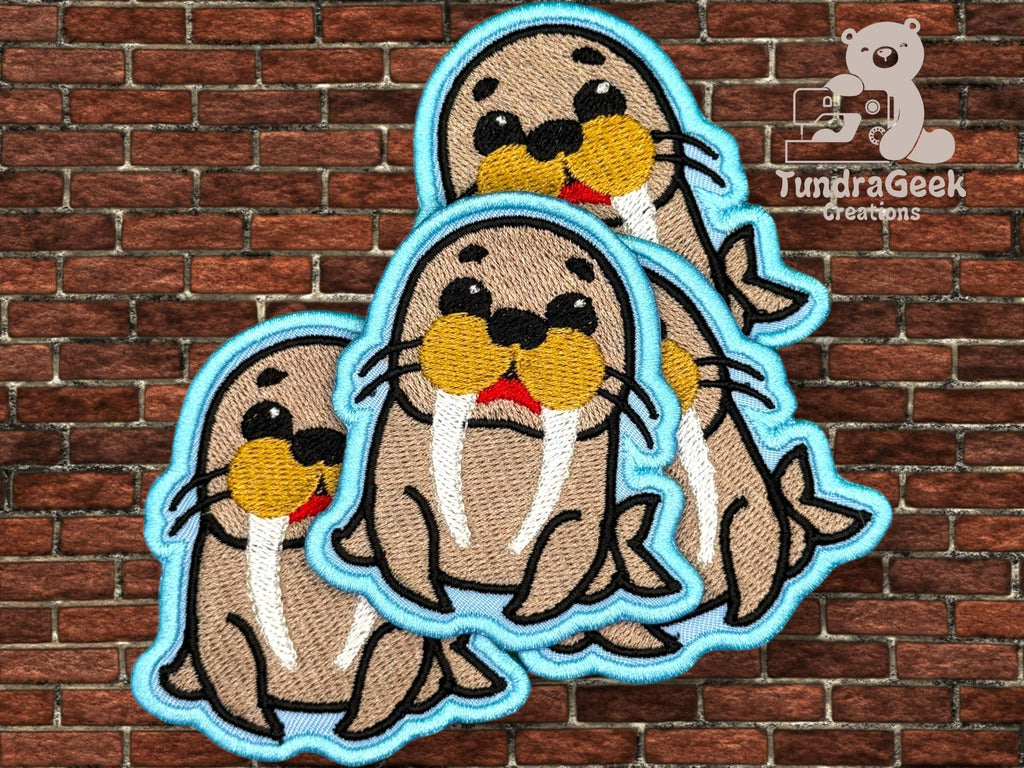 Three embroidered walrus patches with blue borders are arranged in front of a brick wall with the TundraGeek Creations logo in the top right corner.