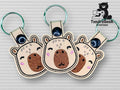 Three embroidered bear face keychains with green metal rings are displayed on a textured white surface. The logo TundraGeek Creations with a bear holding a fish is in the top right corner.
