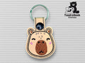 A keychain shaped like a bears head made of stitched fabric with a metal ring, displayed on a textured background, and the TundraGeek Creations logo in the top right corner.