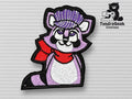 Embroidered patch of a purple raccoon wearing a red scarf and a striped cap, displayed on a textured light background with the TundraGeek Creations logo in the corner.