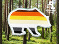 A bear-shaped patch with horizontal stripes in brown, orange, yellow, white, and black is shown against a forest background. The TundaGeek Creations logo appears in the top right corner.