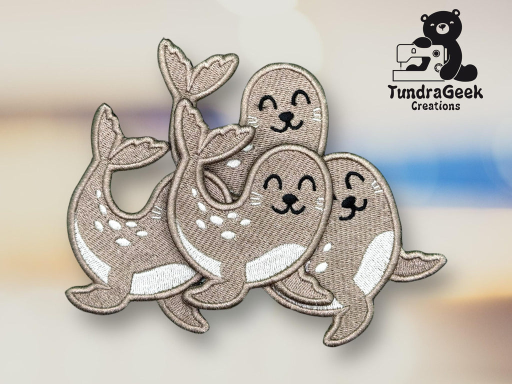 Embroidered patch featuring three smiling cartoon seals with white bellies, overlapping each other. TundraGeek Creations logo with a bear and sewing machine is in the top right corner.