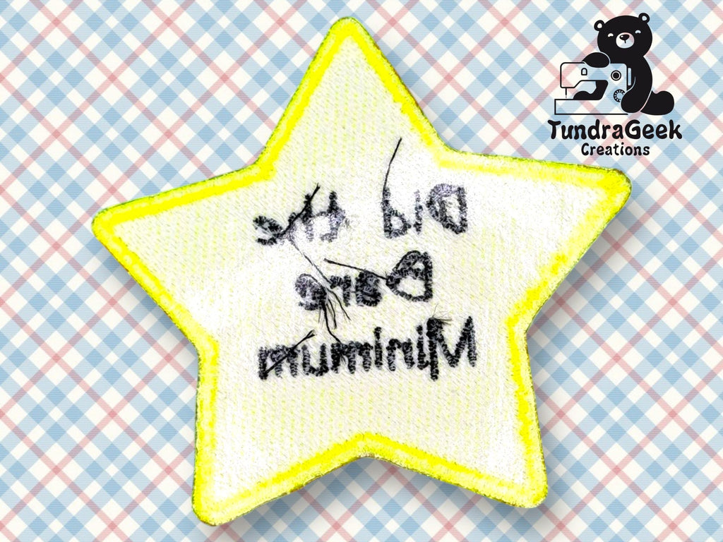 A yellow-edged star-shaped patch with backward text that reads, Did the bare minimum, on a pastel plaid background with a TundraGeek Creations logo in the corner.