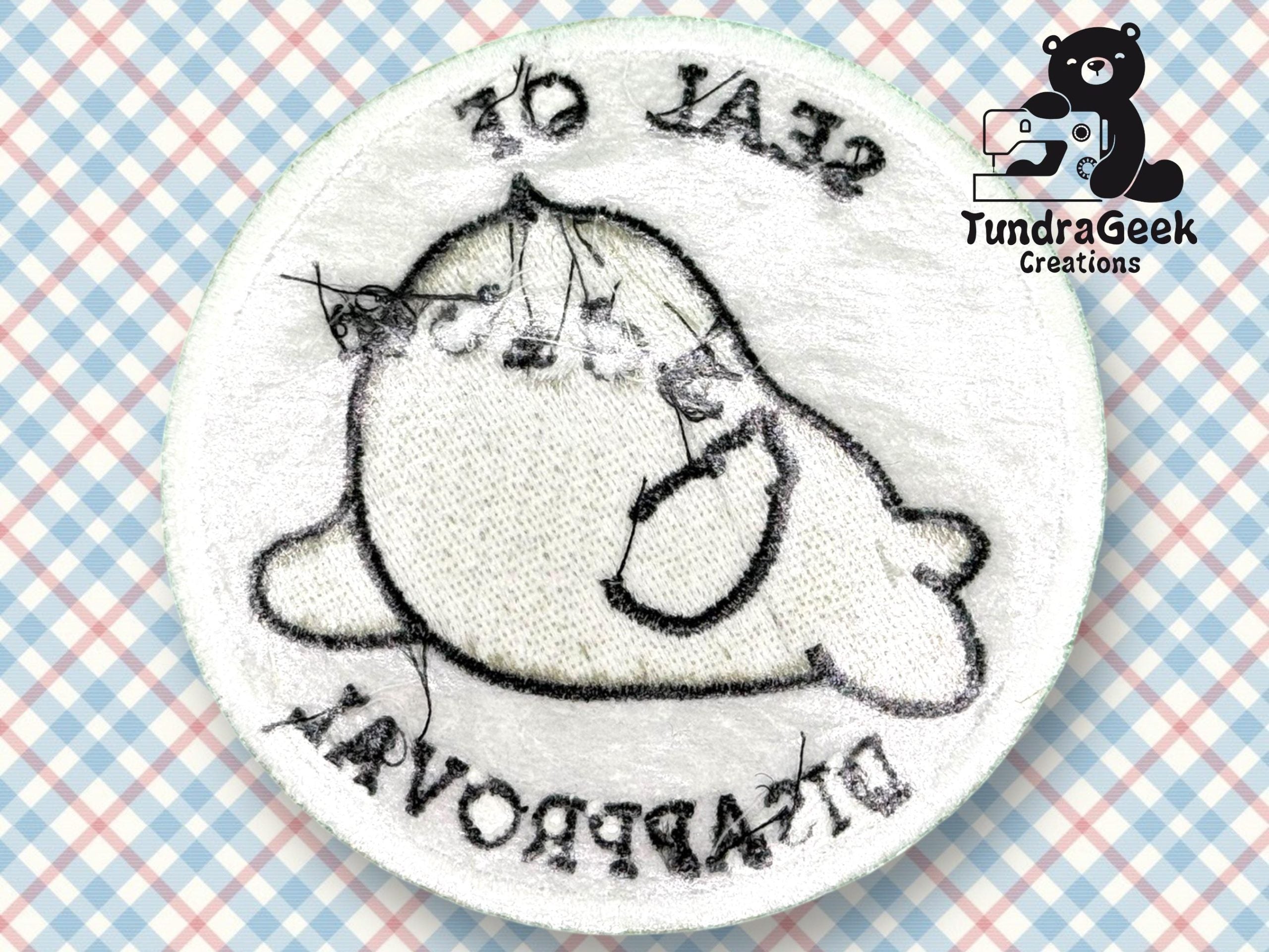 A round embroidered patch features a cartoon seal and the text SEAL OF DISAPPROVAL on a checkered background, with visible thread and needle marks.
