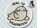An embroidered patch shows a cartoon seal giving a middle finger, with the text SEAL OF DISAPPROVAL above and below the seal.