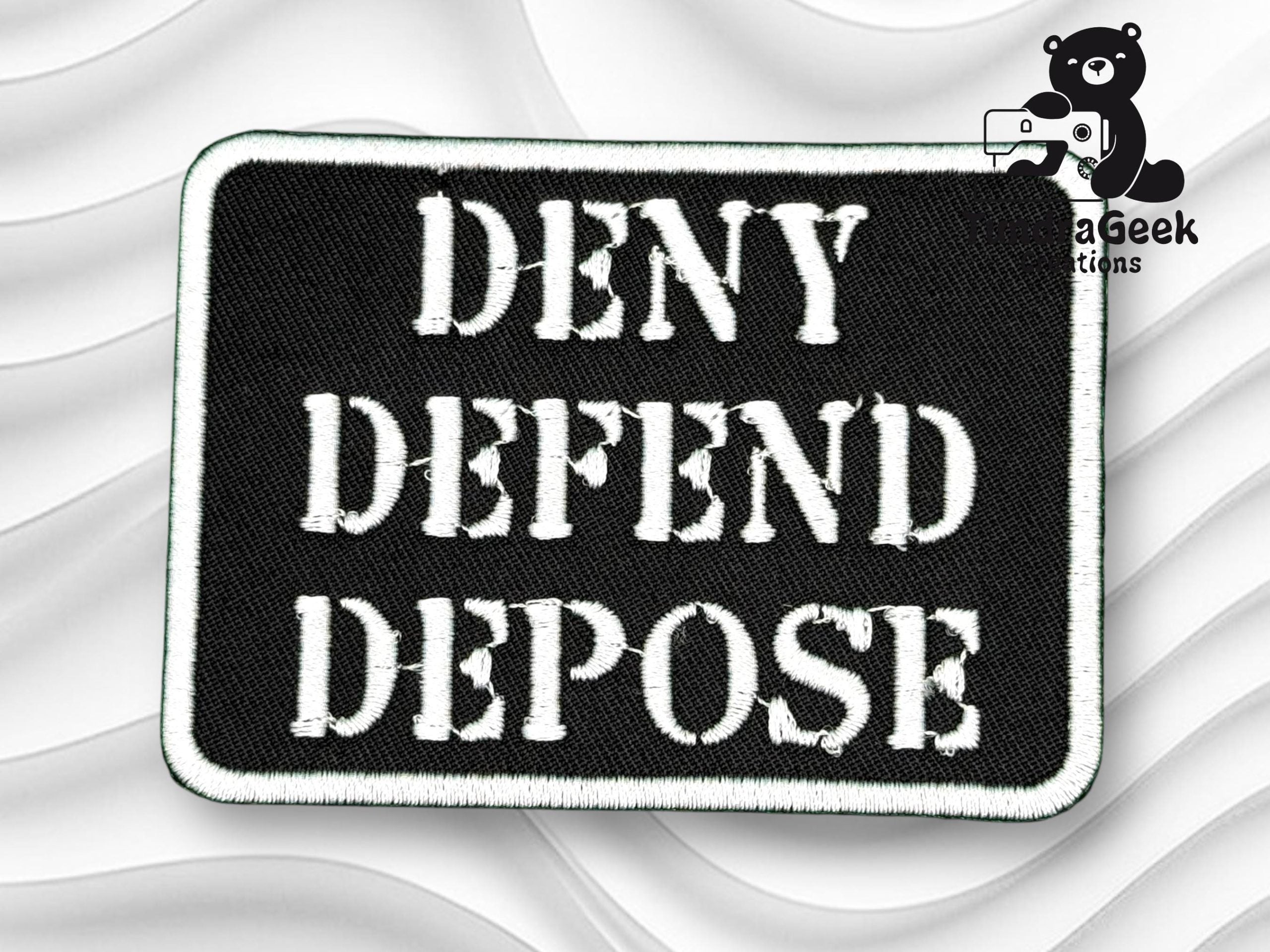 A black rectangular patch with white stitched letters reads DENY DEFEND DEPOSE against a white textured background. A small bear logo with MegaGeek Creations is in the top right corner.