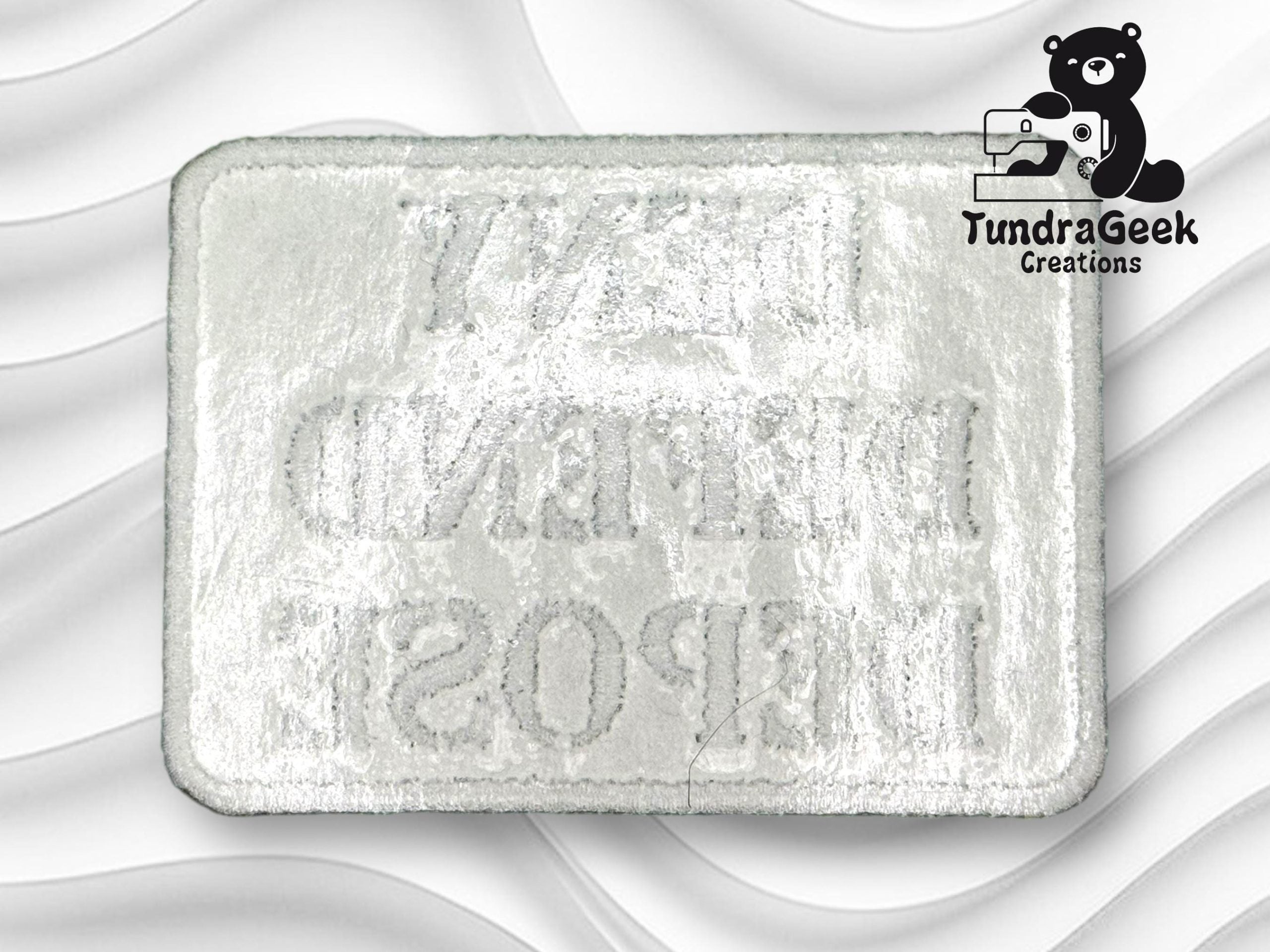 A rectangular embroidered patch with mirrored text on a white background, featuring the TundraGeek Creations logo with a bear holding a sewing machine in the top right corner.