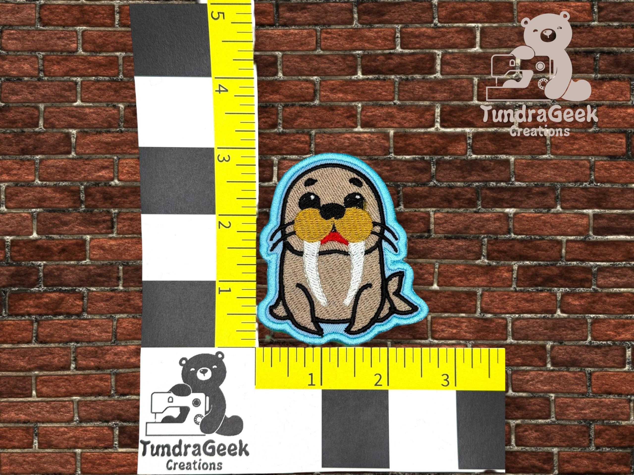 An embroidered walrus patch with blue trim is placed against a brick wall backdrop, next to a ruler showing it measures approximately 3 inches tall and 2.5 inches wide.
