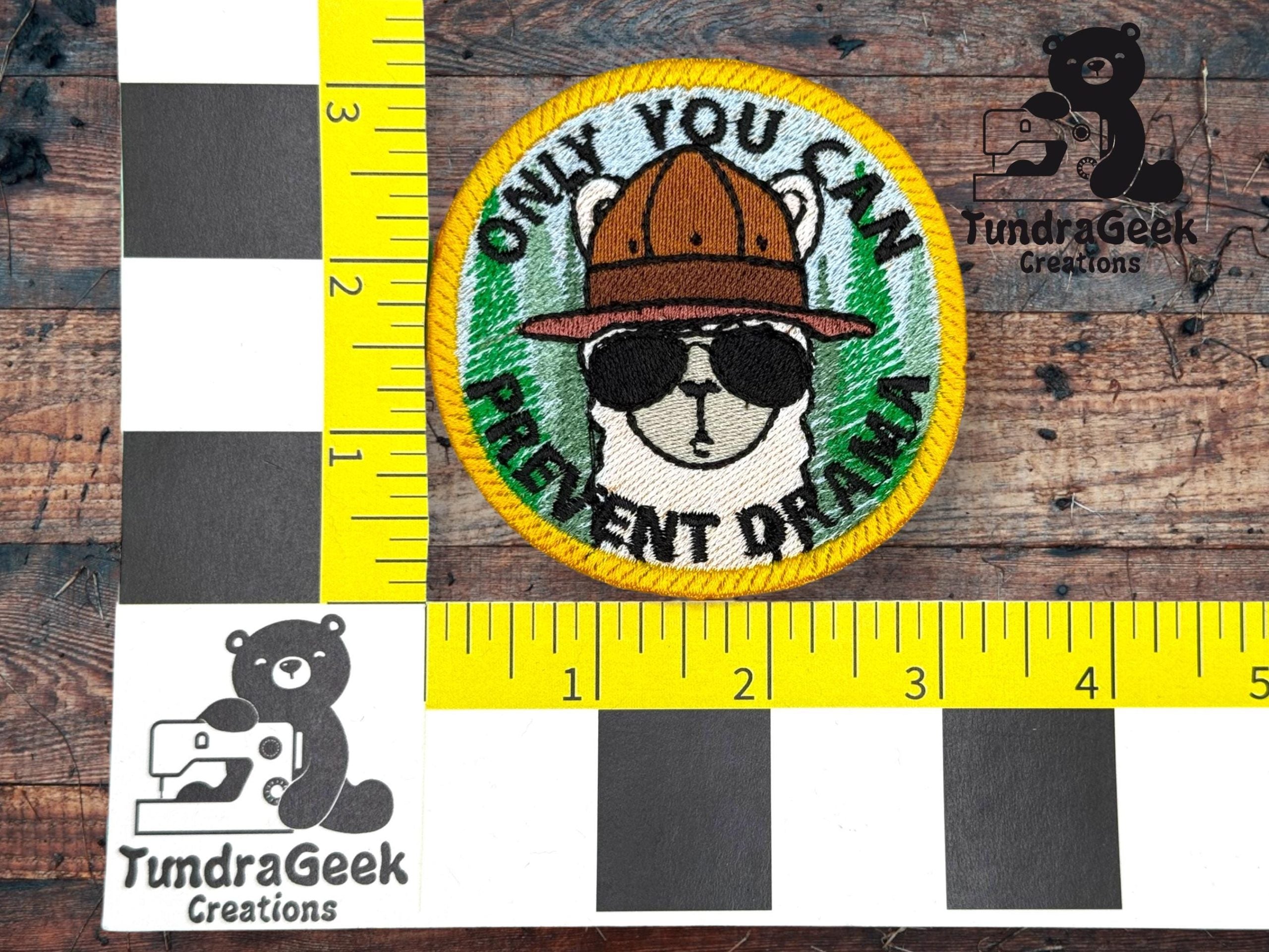 A round embroidered patch features a bear in sunglasses and a hat with the text ONLY YOU CAN PREVENT DRAMA on a green background. Measuring scales and TundraGeek Creations logo are visible.