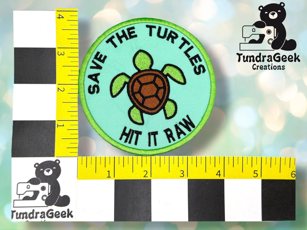 A round patch with a turtle illustration and the text SAVE THE TURTLES HIT IT RAW, placed next to rulers for scale. TundraGeek Creations logo appears in two corners.