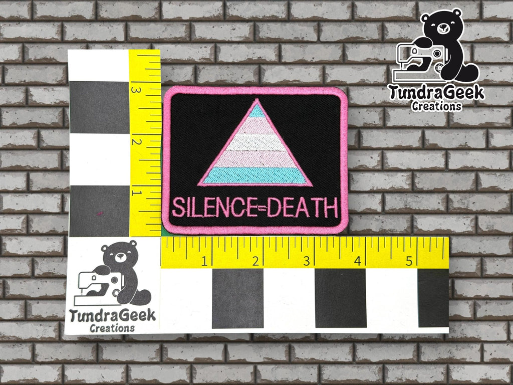 Rectangular patch with a pastel triangle and SILENCE=DEATH text, placed on a measurement grid background with TundraGeek Creations logos.