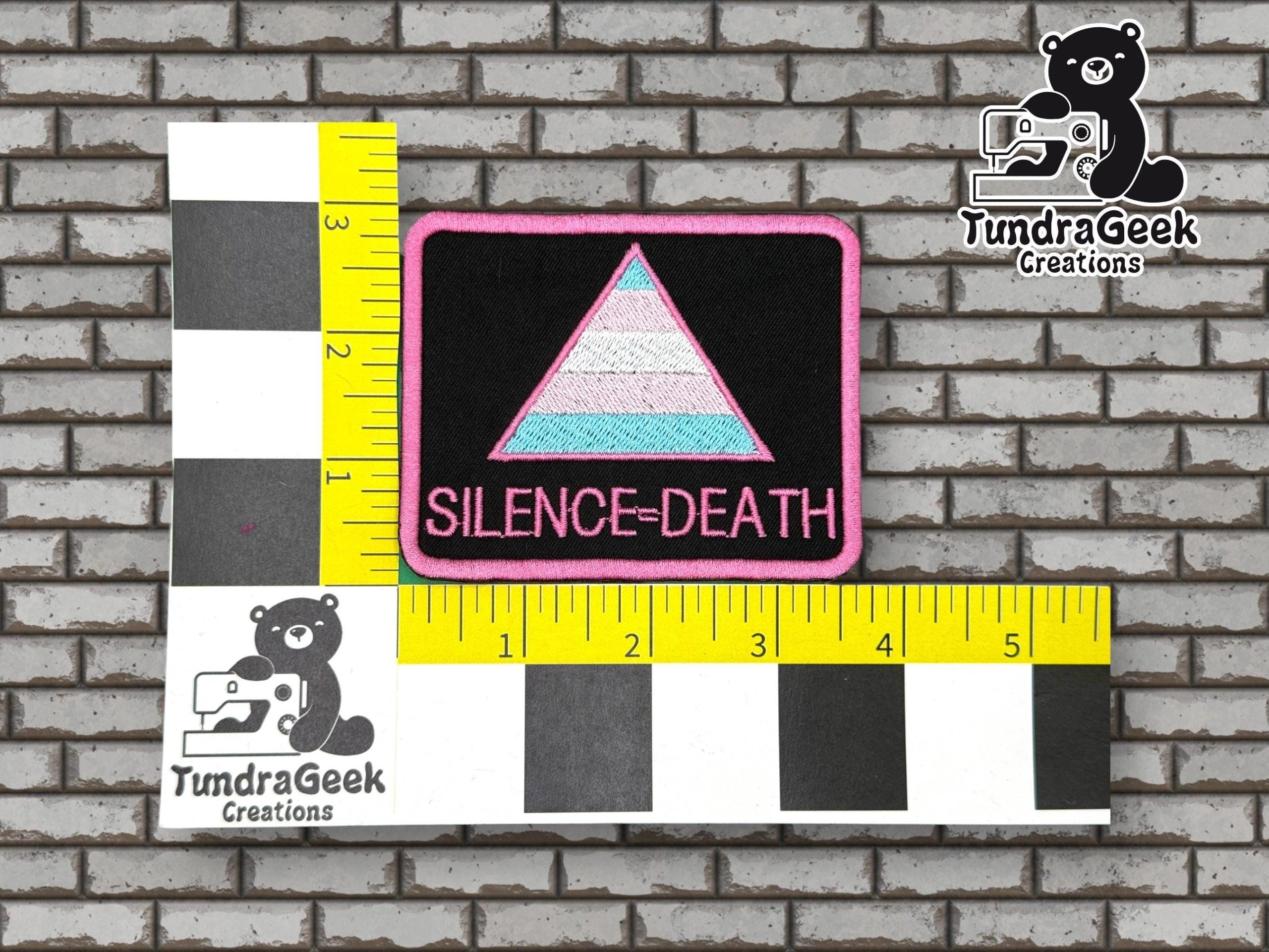 Rectangular patch with a pastel triangle and SILENCE=DEATH text, placed on a measurement grid background with TundraGeek Creations logos.