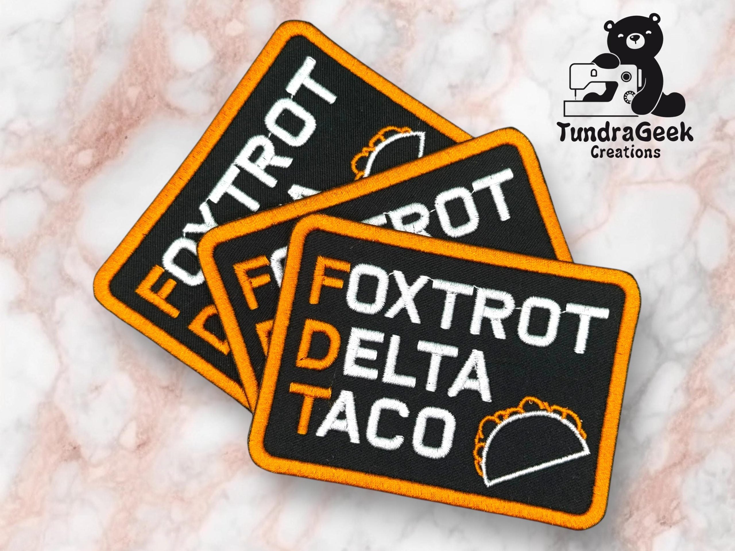 Three rectangular patches read FOXTROT DELTA TACO with the initials FDT highlighted; a taco graphic appears beside the word TACO. TundraGeek Creations logo in upper right corner.